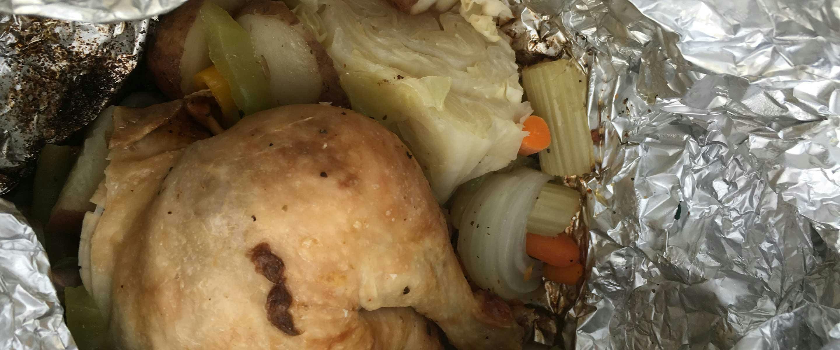 chick and onion and other vegetables roasting over a fire in aluminum foil